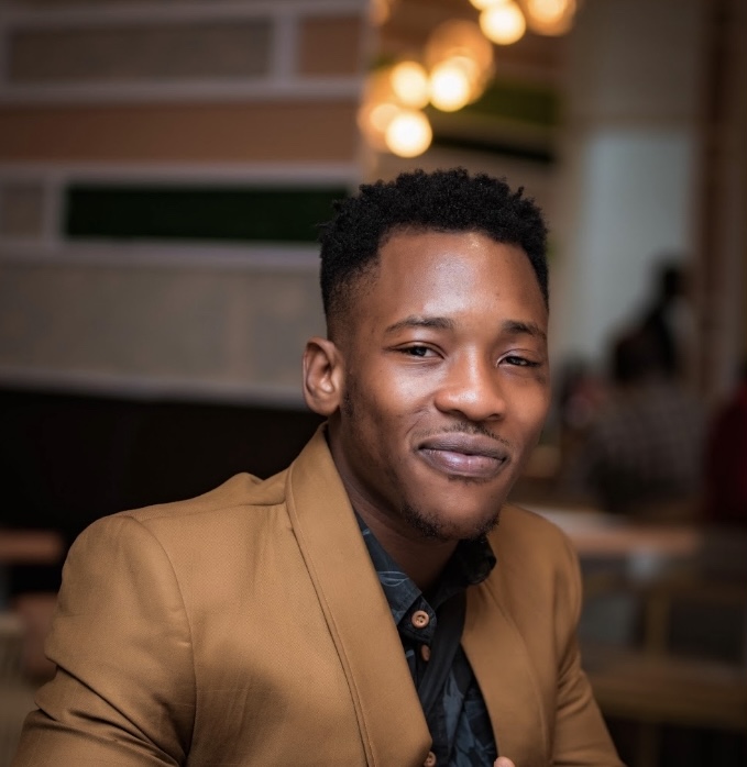 Adeoluwa Adesunloye in a tan jacket, smiling